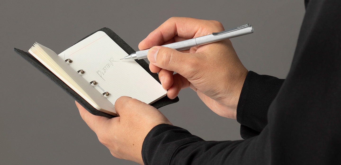 A person holding a pen and writing the word PLOTTER on a ring leather binder.