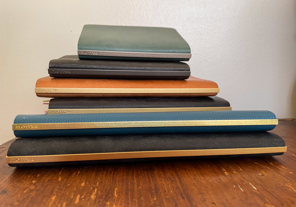 Stack of 6 PLOTTER leather binders that expose their backplate on the spine of the leather binder.