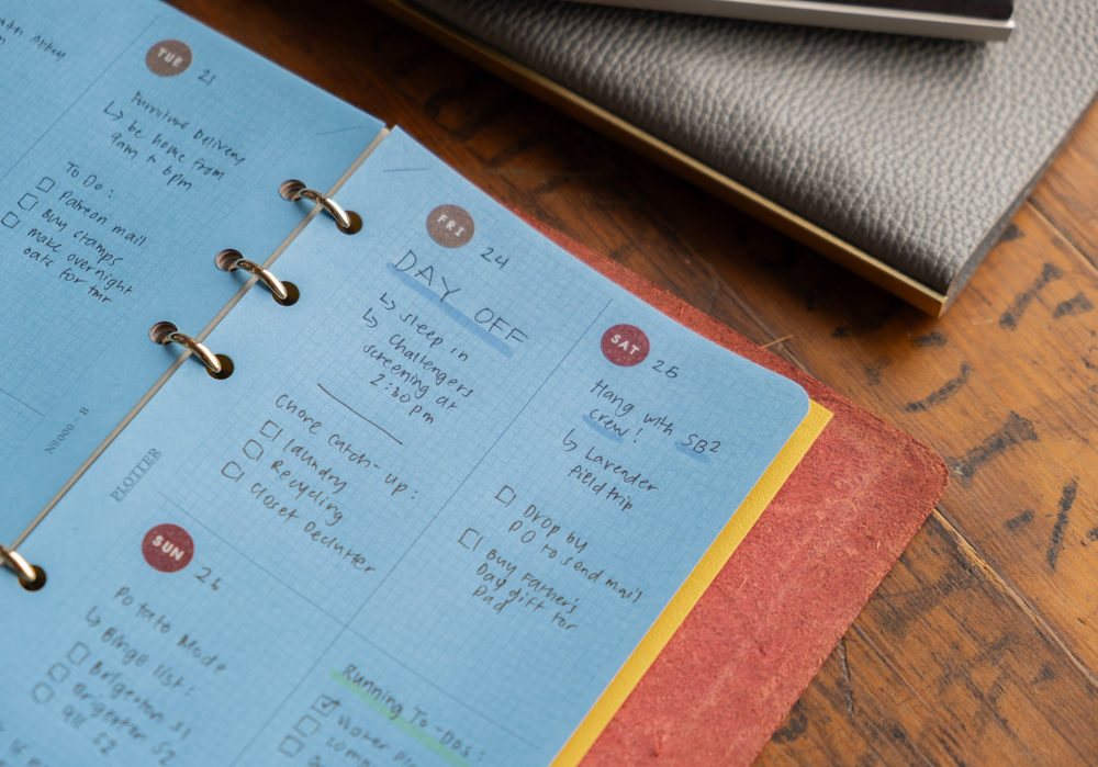 A close-up of the Blue Paper refill paper being used as a weekly schedule inside a PLOTTER leather binder.