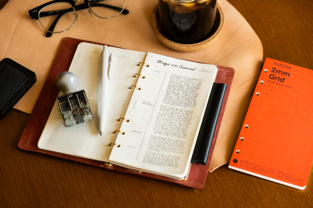 PLOTTER Leather Binder open with notes called "things I learned this year" beside ice coffee, Refill Memo Pad, Pen and eye glasses.