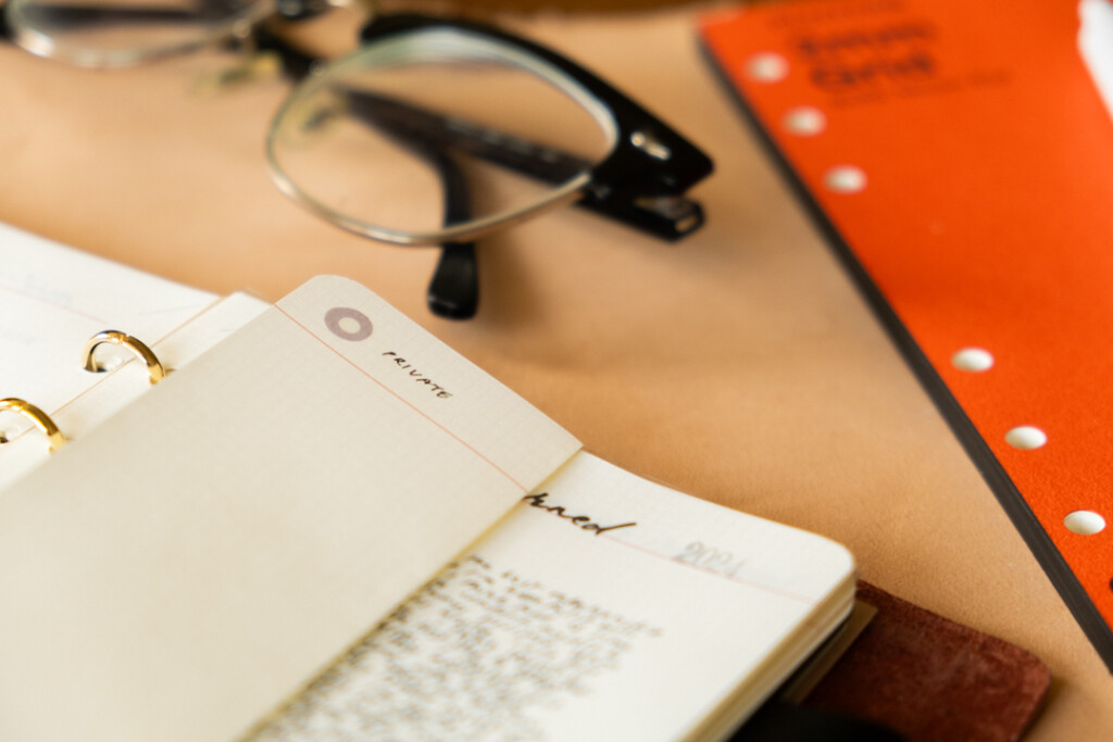 Close-up of PLOTTER Leather Binder open with a folded page beside eye glasses and a PLOTTER Refill Memo Pad.