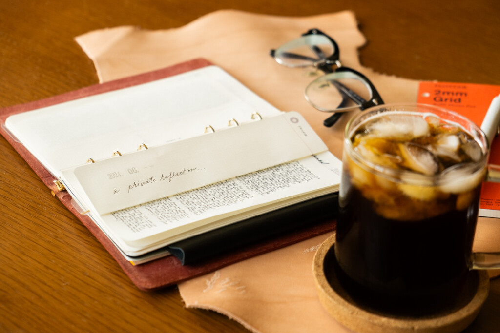 PLOTTER Leather Binder open with a folded page beside ice coffee, and eye glasses.