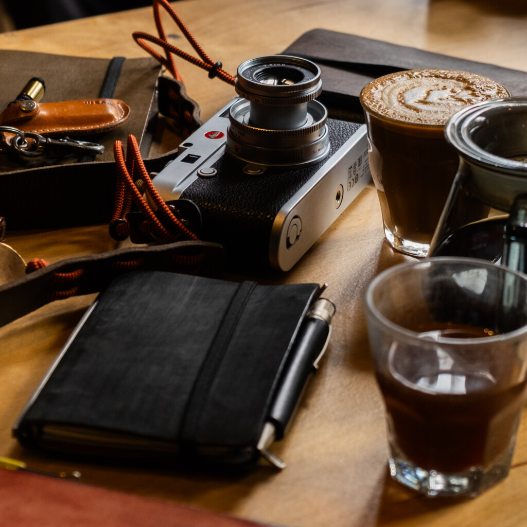 Wooden table with cameras and 3 PLOTTER leather binders and coffee cups.