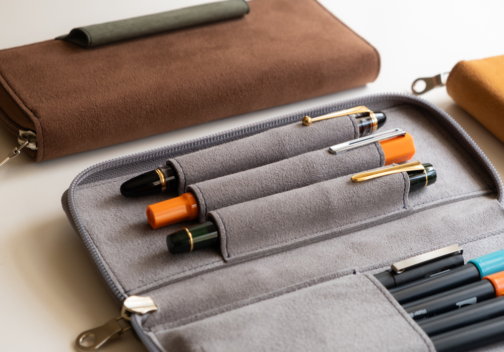 A gray PLOTTER Long Zipper Pen Case filled with three fountain pens. 