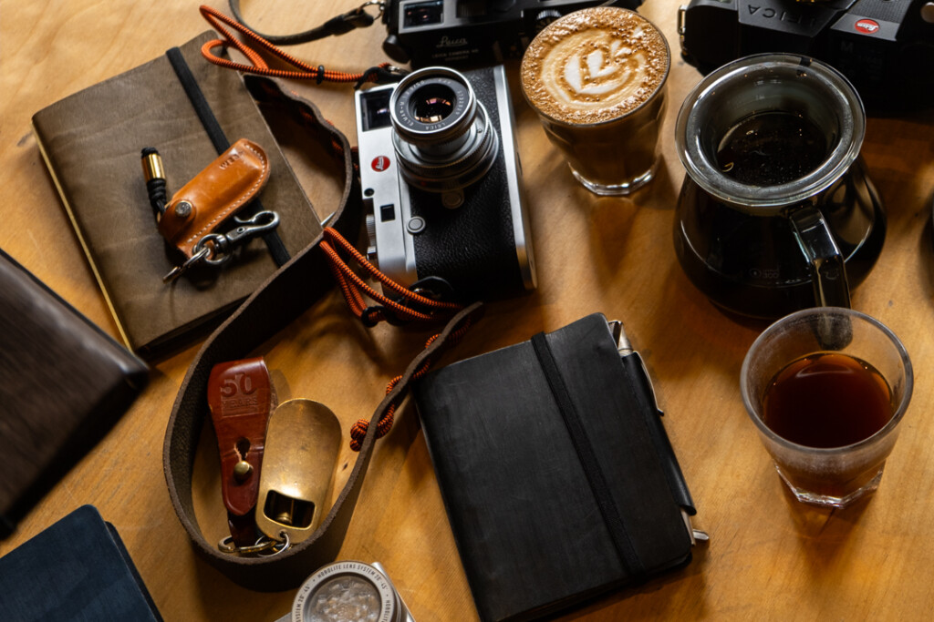 Over-head shot Wooden table with cameras and 3 PLOTTER leather binders and coffee cups.