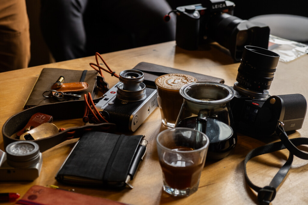 Wooden table with cameras and 3 PLOTTER leather binders and coffee cups.