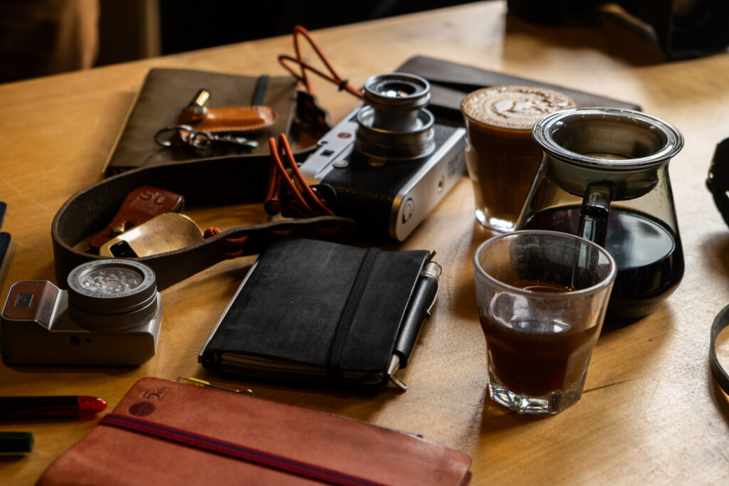 Wooden table with cameras and 3 PLOTTER leather binders and coffee cups.