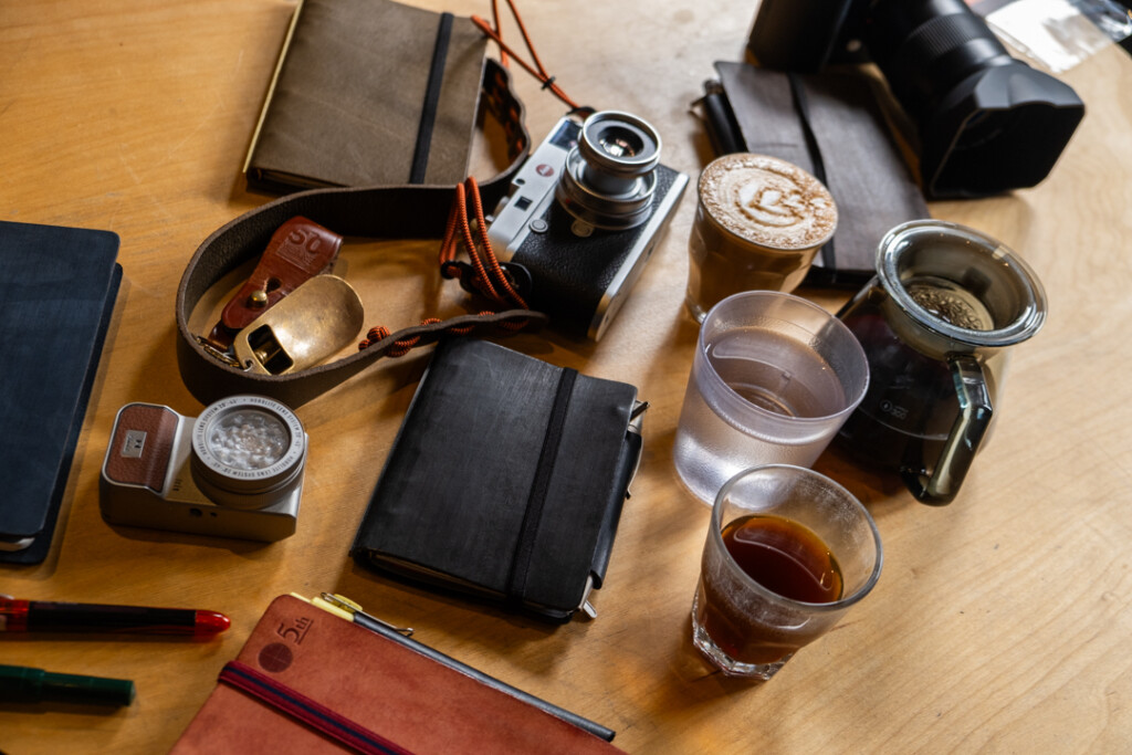 Wooden table with cameras and 3 PLOTTER leather binders and coffee cups.