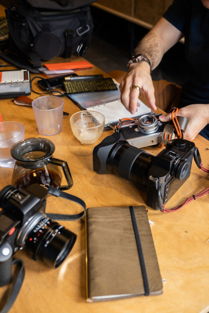 Wooden table with cameras and PLOTTER leather binders and coffee cups.