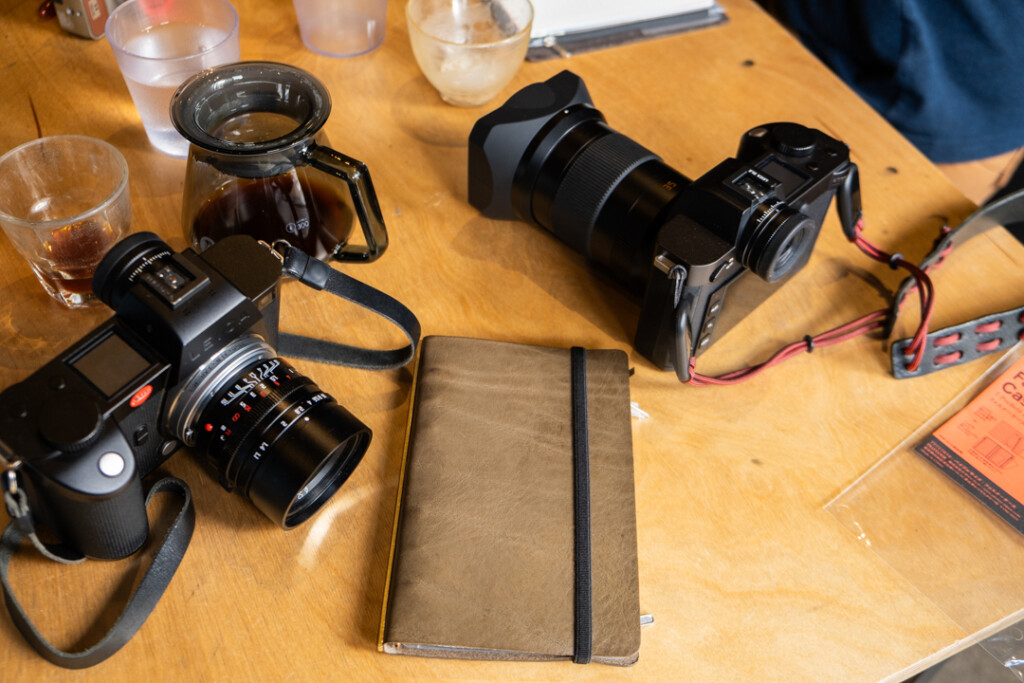 Wooden table with cameras and PLOTTER leather binders and coffee cups.