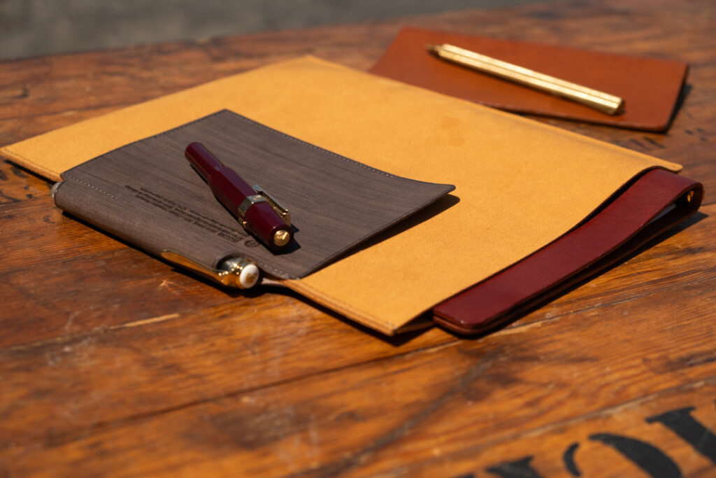 A5 PLOTTER Leather binder case on a wooden table near a PLOTTER Leather Binder and pens.