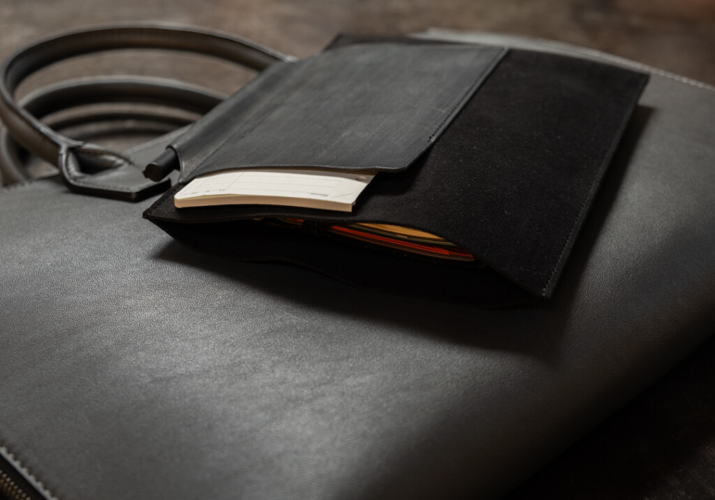 PLOTTER Leather Binder Case Bible Size in black on top of a briefcase on a metal table.