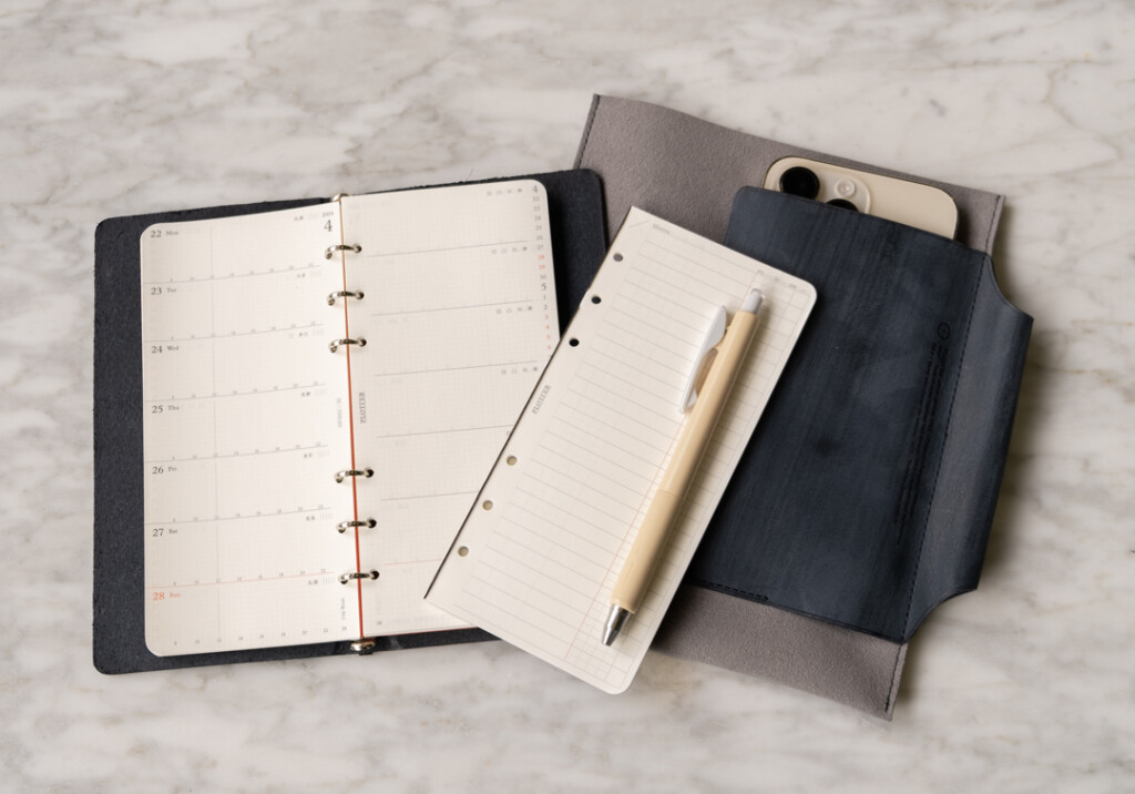 Narrow Size PLOTTER Leather Binder on desk beside a Leather Binder Case in grey and blue which is on white marble table.