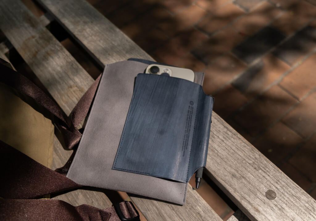 Narrow Size PLOTTER Leather Binder on desk beside a Leather Binder Case in grey and blue which is on park bench.