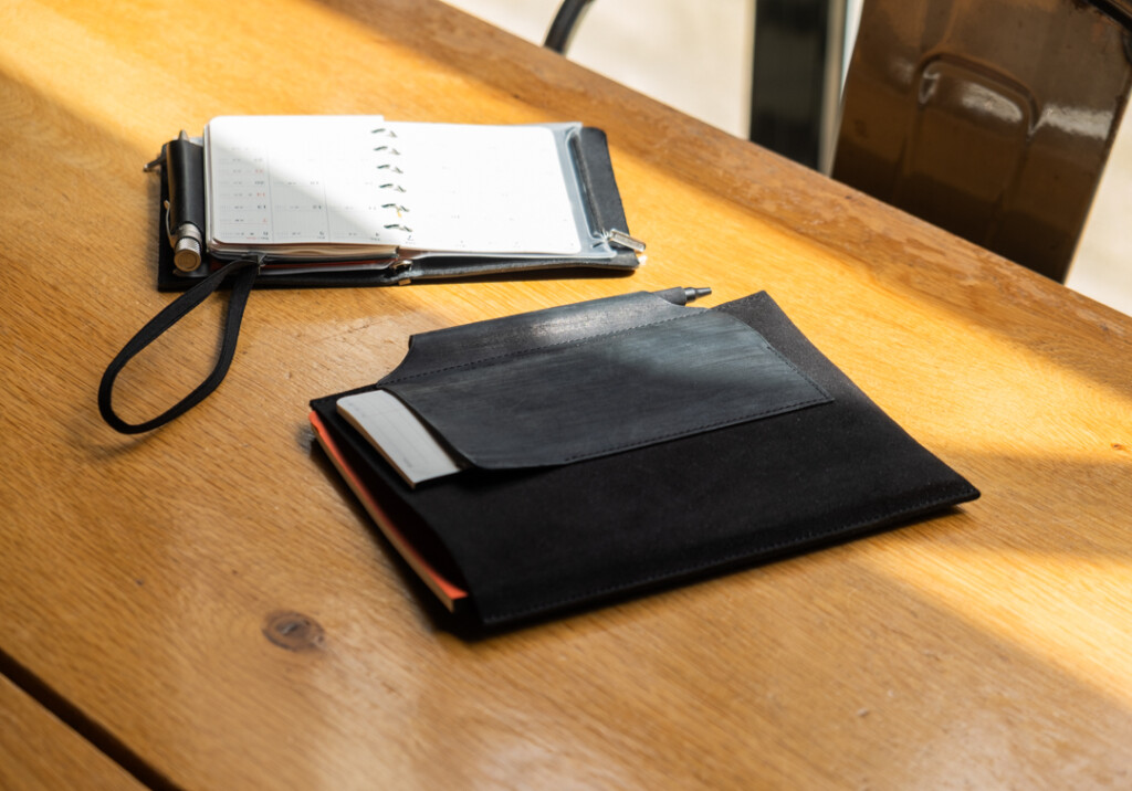 PLOTTER Leather Binder open on desk beside a Leather Binder Case in all black.