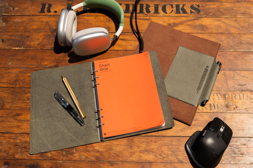 A5 PLOTTER Leather binder open on a wooden table near headphones, Leather BInder Case and a computer mouse.