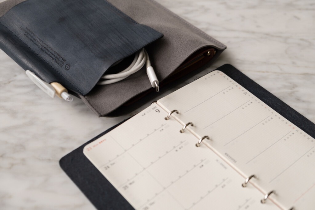 PLOTTER Leather Binder in Narrow Size on desk beside a Leather Binder Case in Bible Size in the Grey and Blue colorway.