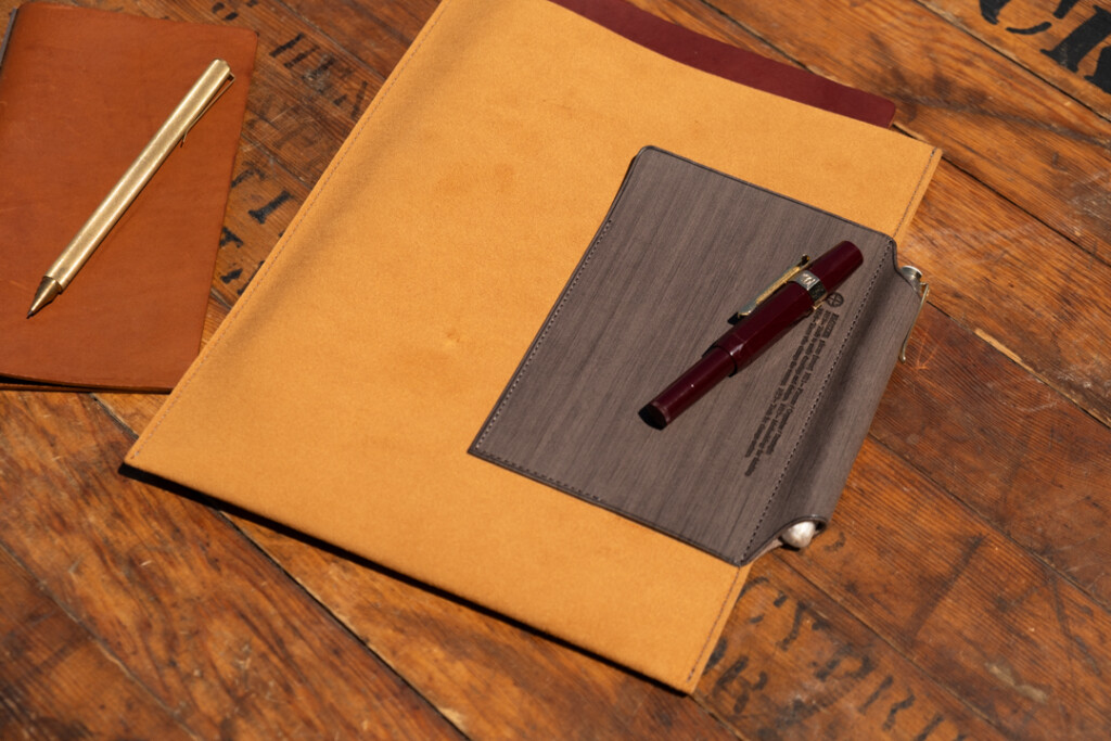 A5 PLOTTER Leather binder case on a wooden table near a PLOTTER Leather Binder and pens.