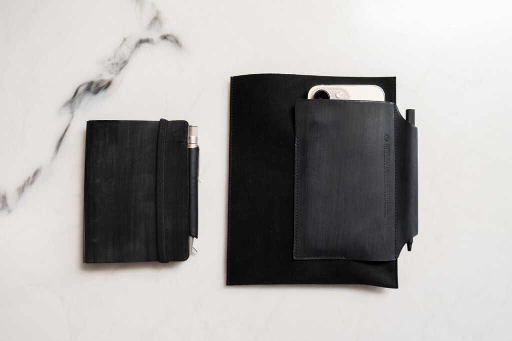 Black PLOTTER Leather Binder in Mini Size on desk beside a Leather Binder Case in Bible Size in the all black color way.