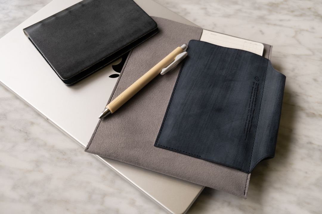 PLOTTER Leather Binder on desk beside a Leather Binder Case in grey and blue which is on top of a closed laptop.