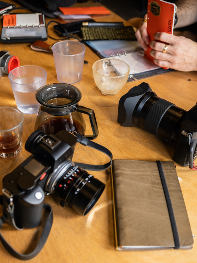 Wooden table with cameras and PLOTTER leather binders and coffee cups.