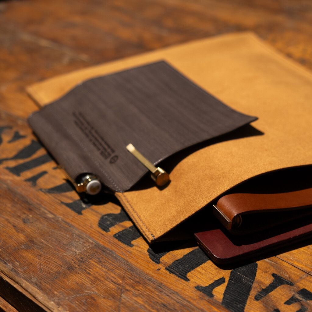 A5 PLOTTER Leather binder case on a wooden table with a PLOTTER Leather Binder and pens.