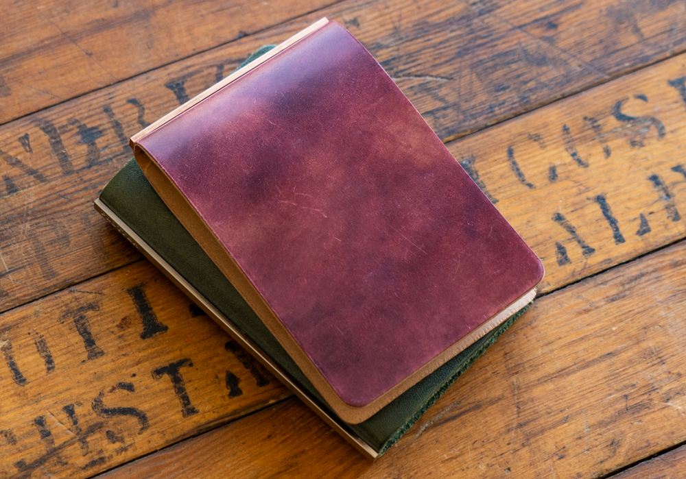 A 3-Ring Leather Binders in Unevenly Dyed Cordovan stacked on top of a PLOTTER Mini 5 Leather Binder.