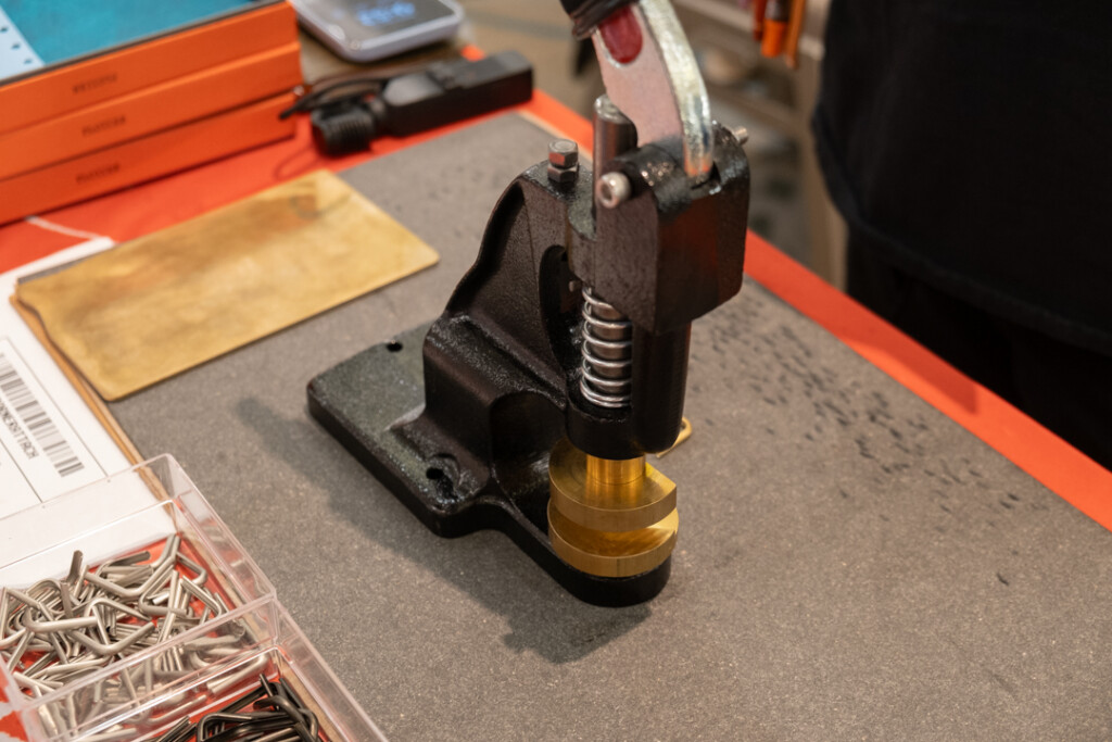 PLOTTER USA corner hardware machine beside other tools and PLOTTER Leather Binders on a table.