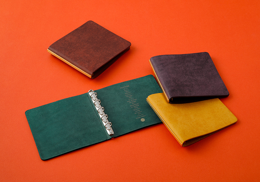 Four 5-Ring Leather Binders in Mini 5 Size (in colors of Wine, Blue green, Purple, and Yellow) against an orange background.