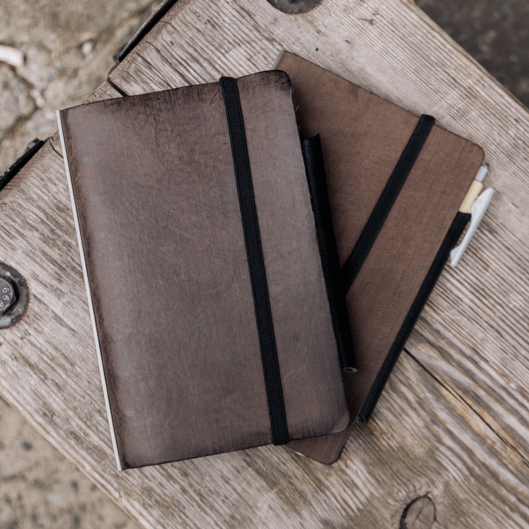 Two Gray PLOTTER Leather Binders in Horse Hair II Leather in Bible Size on wooden table.