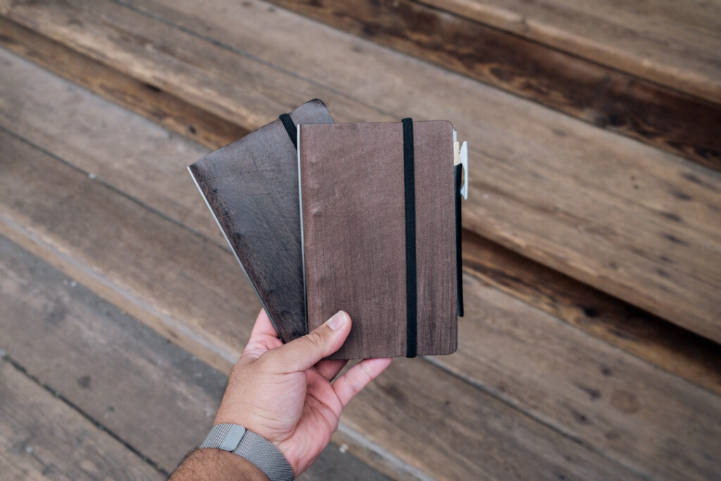 Man holding two Gray PLOTTER Leather Binders in Horse Hair II Leather in Bible Size in front of wooden stairs.