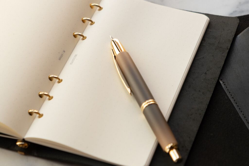 Close up of PLOTTER Leather leather binder in Bible Size with a fountain pen resting on top of the open binder.