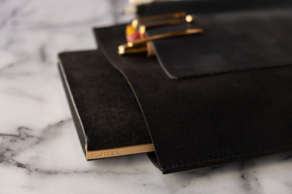 Close up of PLOTTER Leather Binder Case in Bible Size in Black which has fountain pens stored on the front leather pocket, on a marble table.