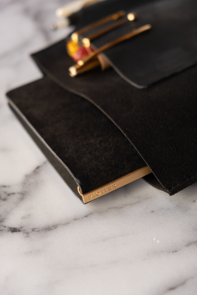 Close up of PLOTTER Leather Binder Case in Bible Size in Black which has fountain pens stored on the front leather pocket, on a marble table.