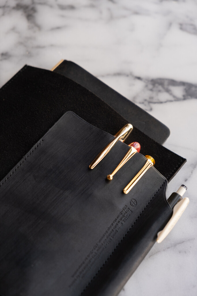 Close up of PLOTTER Leather Binder Case in Bible Size in Black which has fountain pens stored on the front leather pocket, on a marble table.