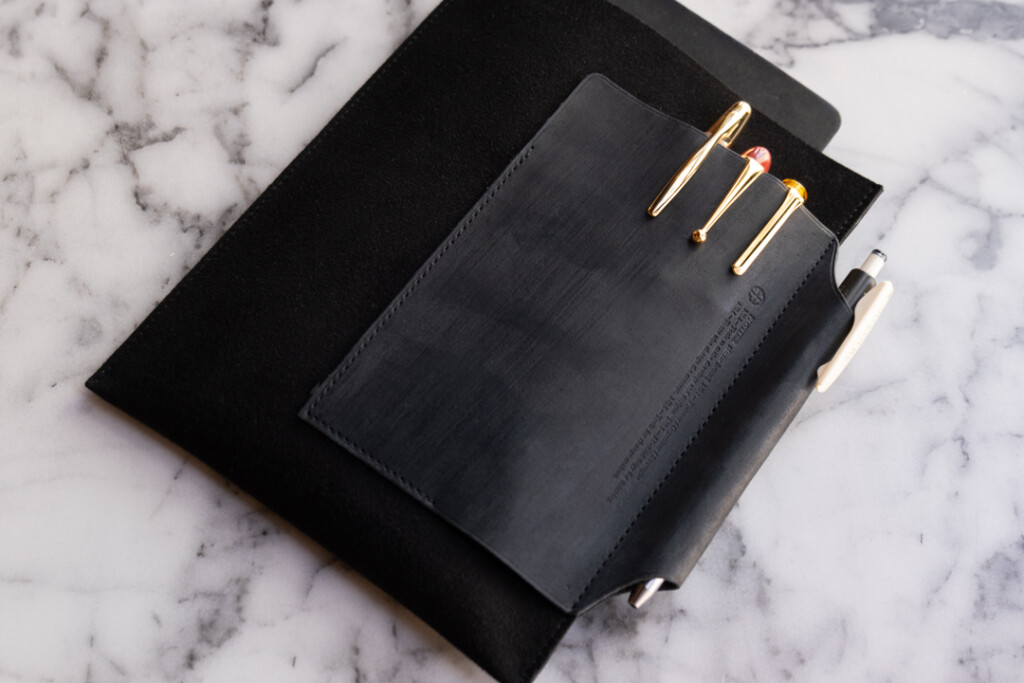 PLOTTER Leather Binder Case in Bible Size in Black which has fountain pens stored on the front leather pocket, on a marble table.