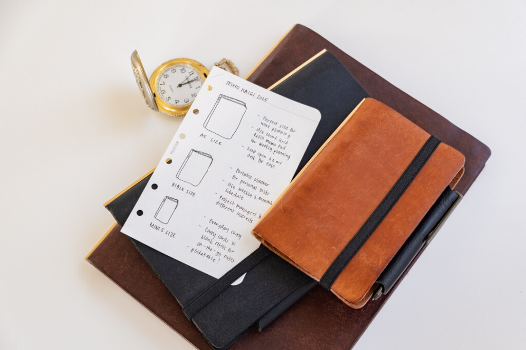 A stack of PLOTTER Leather Binders with a vintage stop watch beside one of the binders.