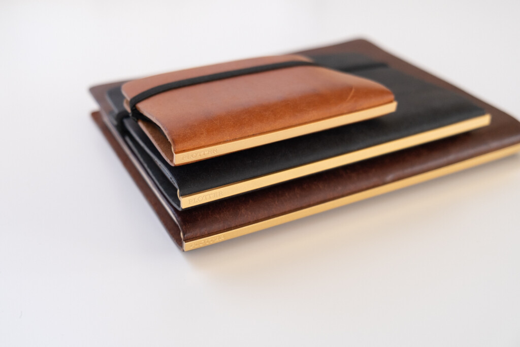 A stack of 3 PLOTTER Leather Binders consisting of: a black Bible Size PLOTTER, a brown A5 Size PLOTTER, and a beige Mini 5 Size PLOTTER.