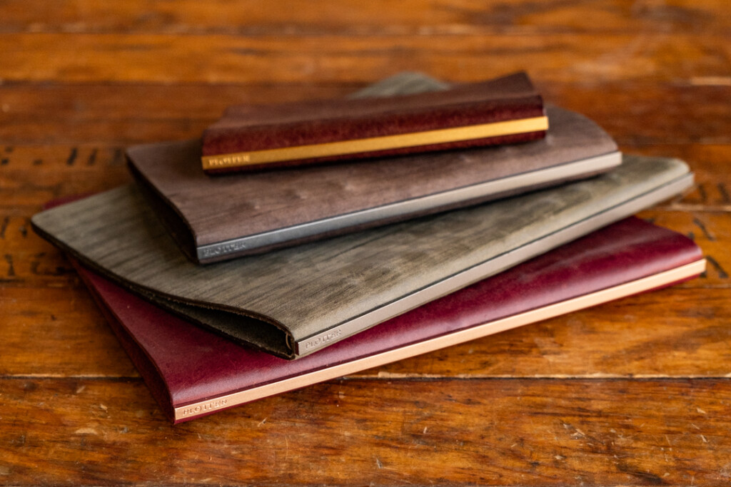 Stack of PLOTTER Leather Binders in various sizes on a wooden table.