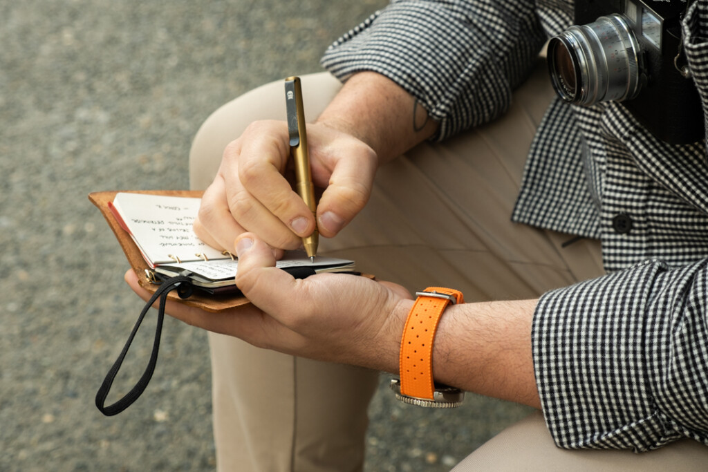 A person writing in an PLOTTER Mini 5 Size Leather Binder with a brass pen.