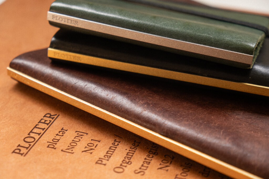 Close-up of a stack of PLOTTER Leather Binders in various sizes on a beige leather surface.