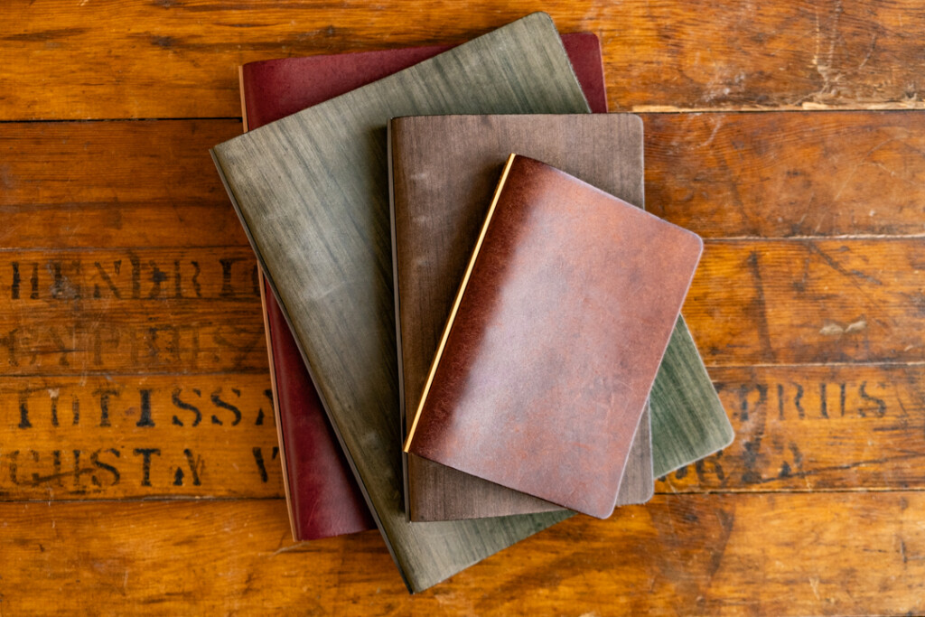 Over-head view of a stack of PLOTTER Leather Binders in various sizes on a wooden table.