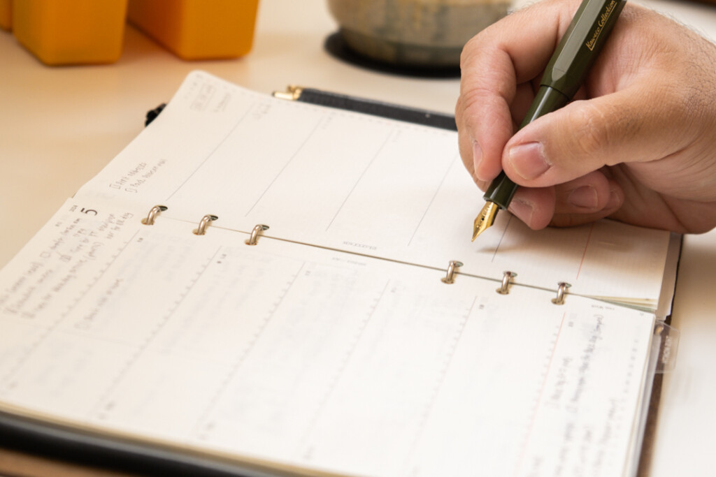 Close-up of a person writing in an PLOTTER A5 Size Leather Binder with a green fountain pen.