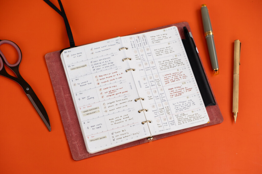 Bible Size PLOTTER open to a weekly schedule with plans and events written in pen on an orange table background.