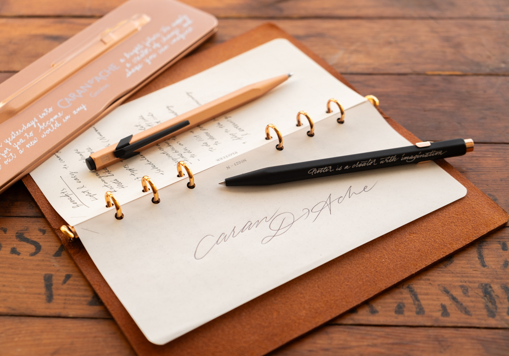 Two CARAN D'ACHE ballpoint pens alongside a PLOTTER Leather Binder in Bible Size.