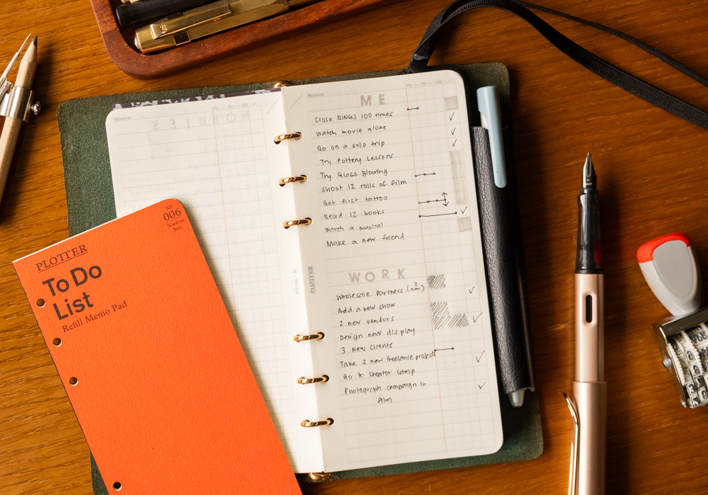 A PLOTTER Narrow Size Leather Binder open to a List of new year's work and personal goals. There is a fountain pen and other writing utensils near the PLOTTER.