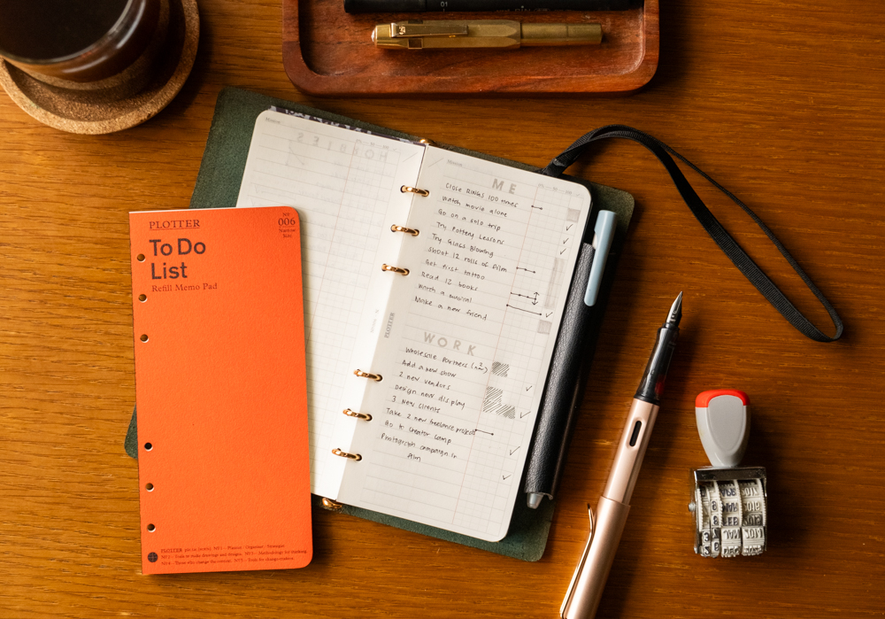 A PLOTTER Narrow Size Leather Binder open to a List of new year's work and personal goals. There is a fountain pen and other writing utensils near the PLOTTER.