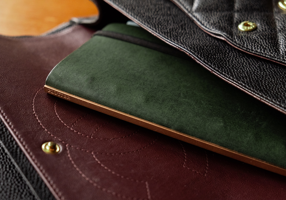 A green PLOTTER Narrow Size Leather Binder inside a black leather hand bag.