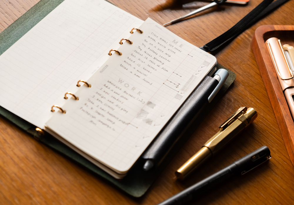 A close up of a PLOTTER Narrow Size Leather Binder open to a List of new year's work and personal goals. There is a fountain pen and other writing utensils near the PLOTTER.