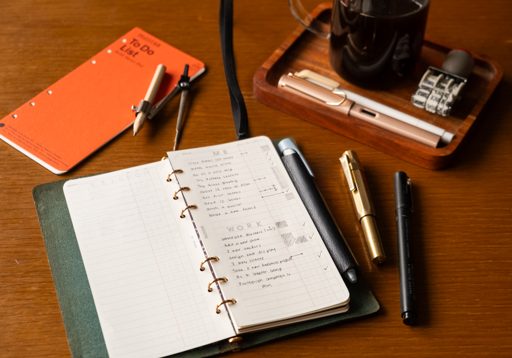 A PLOTTER Narrow Size Leather Binder open to a List of new year's work and personal goals. There is a fountain pen and other writing utensils near the PLOTTER.